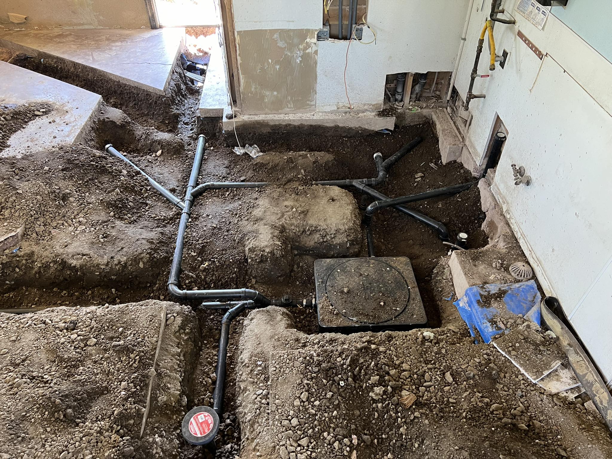 Exposed plumbing pipes and dirt trenches in a partially demolished room, indicating ongoing plumbing or construction work inside a building.